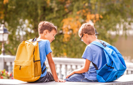 Bild på två skolpojkar med varsin ryggsäck som sitter och pratar med varandra på skolgården